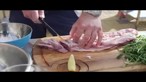 Person's-hands-cutting-a-piece-of-raw-meat-using-a-butcher's-knife-on-a-wooden-surface-outside.-Barbeque-preparation.-shot-in-4k