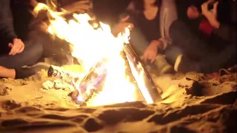 Close-Up-view-of-the-bonfire-late-at-night.-Young-people-sitting-by-the-fire-in-the-evening.-Cheerful-friends-singing-songs-and