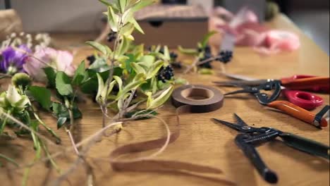 View-from-above:-wooden-table-with-flowers,-scissors,-tapes,-decorating-paper-and-other-tools-for-bouquet-arrangement-at