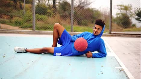 Junger-Afroamerikaner-Liegt-Auf-Dem-Boden-Des-Spielfeldes-Und-Spielt-Mit-Basketballball.-Zeitlupenaufnahme