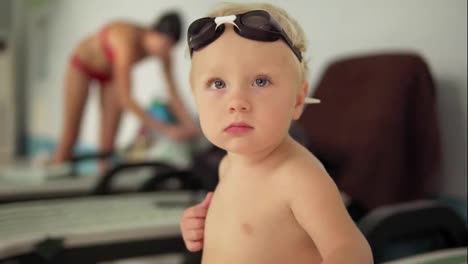 Portrait-of-a-beautiful-toddler-with-goggles-sitting-by-the-pool-and-looking-in-the-camera-waiting-for-his-mother-to-come