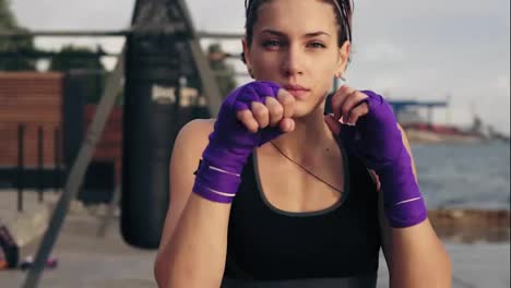 Slow-Motion-shot:-Close-Up-view-of-a-young-woman-shadowboxing-with-her-hands-wrapped-in-boxing-tapes-looking-in-the-camera
