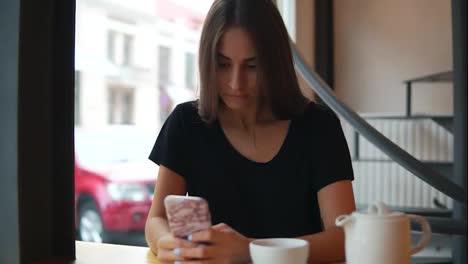 Concentrated-young-lady-with-long-hair-and-natural-makeup-using-her-mobile-phone-in-the-coffee-shot.-Modern-devices-usage