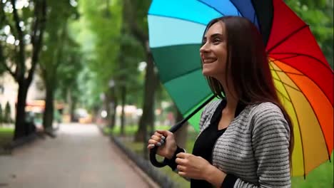 Portrait-of-a-young-smiling-woman-spinning-her-colorful-umbrella-and-taking-it-away-because-it-is-not-raining-anymore-looking-in