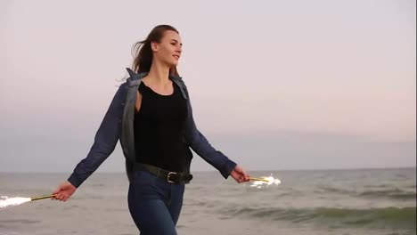 Young-beautiful-woman-running-by-the-sea-during-sunset-and-holding-burning-sparkling-candles-in-both-hands.-Slow-Motion-shot