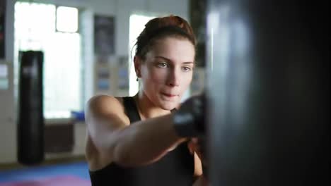 Close-Up-view-of-caucasian-female-boxer-hitting-the-boxing-bag-with-her-hands-in-gloves-in-the-gym-alone.-Tough-power-training-of