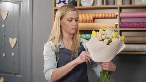 Female-blonde-florist-arranging-modern-bouquet-and-choosing-the-perfect-riband-for-it-combining-different-colors.-Handsome