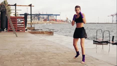 Mujer-Joven-Atlética-Haciendo-Boxeo-De-Sombras-Junto-Al-Mar.-Hermosa-Boxeadora-Entrenando-En-La-Playa-Por-La-Mañana,-Lanzando-Golpes