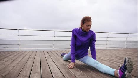 Athletic-woman-stretching-her-legs-before-a-jog-on-the-beach-by-the-sea-early-in-the-morning.-Young-girl-doing-splits.-Training