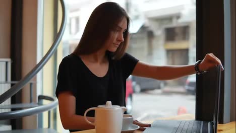 Young-woman-sitting-in-the-coffee-shot-having-a-coffee-break,-she-is-opening-her-laptop-and-starts-working-and-surfing-in-the