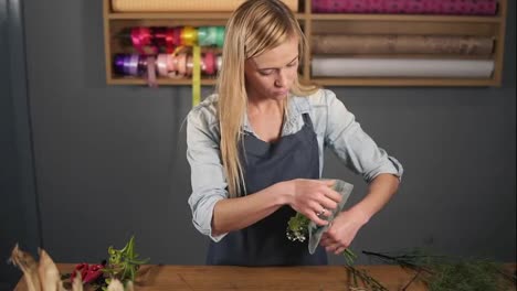 Young-beautiful-female-florist-wrapping-a-bunch-of-flowers-in-decorating-paper.-Slow-Motion-shot