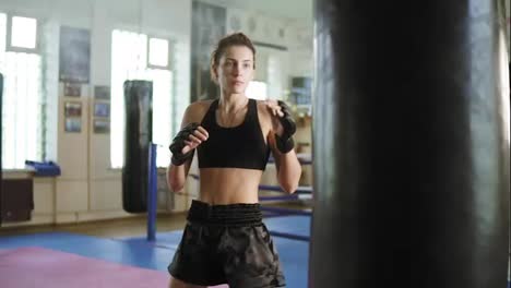 Close-Up-view-of-caucasian-female-kickboxer-hitting-the-punching-bag-with-her-hands-and-legs-in-the-gym-alone.-Tough-power