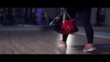 Close-Up-view-of-legs-of-young-fit-woman-entering-a-fitness-club-with-a-bag-and-boxing-gloves-and-preparing-for-the-training-in-a