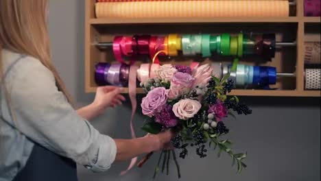 Back-view-of-female-blonde-florist-arranging-modern-bouquet-and-choosing-the-perfect-riband-for-it-combining-different-colors