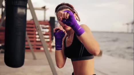 Close-Up-view-of-a-young-woman-shadowboxing-with-her-hands-wrapped-in-purple-boxing-tapes-looking-in-the-camera.-Beautiful