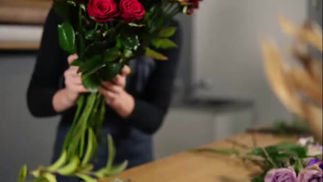 Young-attractive-female-florist-arranging-bouquet-of-beautiful-red-roses-at-flower-shot.-Slow-Motion-shot