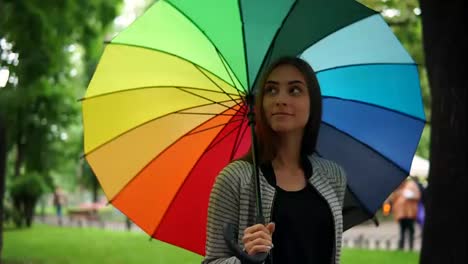 Portrait-of-a-young-attractive-brunette-woman-walking-and-spinning-her-colorful-umbrella-in-a-rainy-day-in-the-city-park