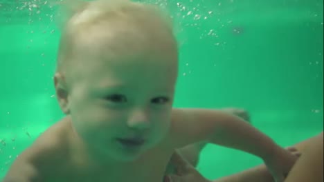 Das-Süße-Blonde-Kleinkind-Schwimmt-Im-Schwimmbad-Unter-Wasser,-Bis-Seine-Mutter-Ihm-Hilft,-Herauszukommen.-Und-Unterwasseraufnahme