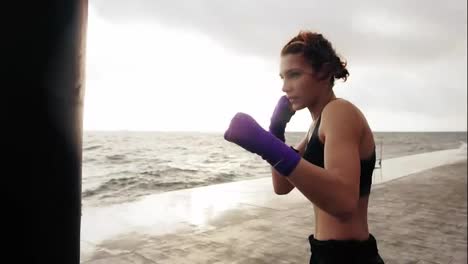 Close-Up-view-of-a-young-woman-training-with-the-boxing-bag-against-the-son.-Her-hands-are-wrapped-in-purple-boxing-tapes