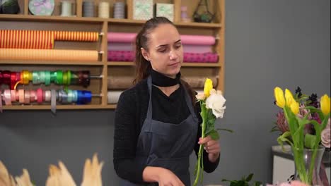 Slow-Motion-shot-of-young-female-florist-arranging-modern-bouquet-at-flowers-shot.-She-combines-creamy-roses-and-yellow-tulips