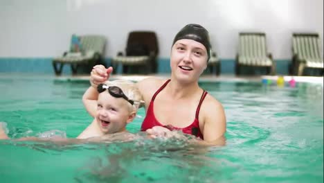 Slow-Motion-shot-of-happy-smiling-little-kid-swimming-together-with-his-mother-in-the-swimming-pool.-Young-mother-is-turning-him