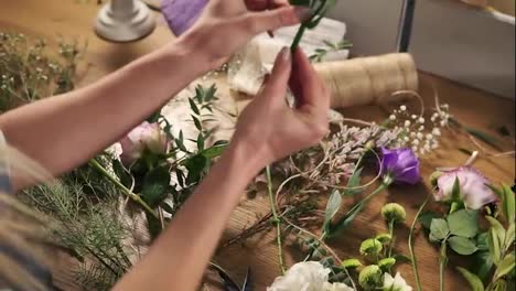 Young-female-blonde-florist-preparing-flowers-for-bouquet.-Hands-of-flower-shot-owner-working-at-her-flower-shot-making-bouquet