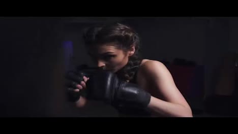 Young-woman-in-boxing-gloves-training-with-a-punching-bag-in-a-boxing-club
