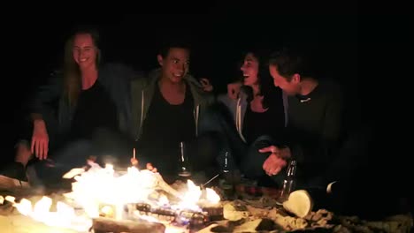 Diverse-group-of-people-sitting-together-by-the-fire-late-at-night-and-embracing-each-other.-Cheerful-friends-talking-and-having