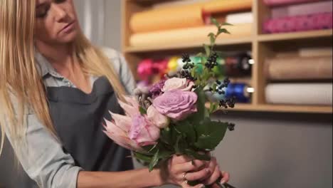 Young-female-blonde-florist-arranging-modern-bouquet-and-looking-how-the-flowers-are-combined.-Handsome-flower-shot-owner