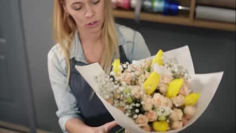 Young-blonde-female-florist-wrapping-a-bunch-of-flowers-in-decorating-paper