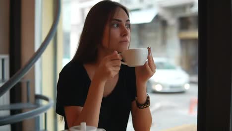 Beautiful-young-woman-dreaming-with-cup-of-hot-coffee-over-window-in-the-coffee-shot.-Break-after-long-busy-day.-Relaxation-with