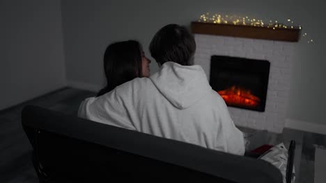 Unrecognizable-couple-sitting-at-home-by-the-fireplace-embraced