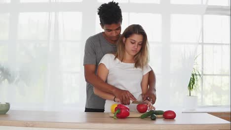 Handsome-african-guy-is-embracing-caucasian-girlfriend-while-helping-her-to-prepare-food-in-the-kitchen-in-the-morning.-Happy