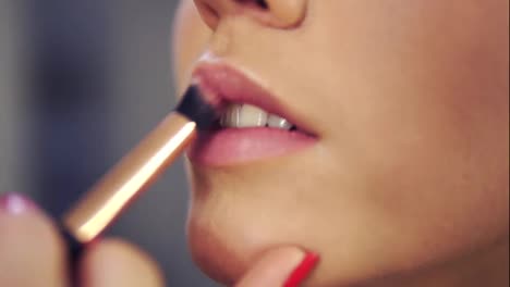 Professional-makeup-artist-applying-lipstick-primer-on-lips-of-model-working-in-beauty-fashion-industry.-Close-Up-view-of-and