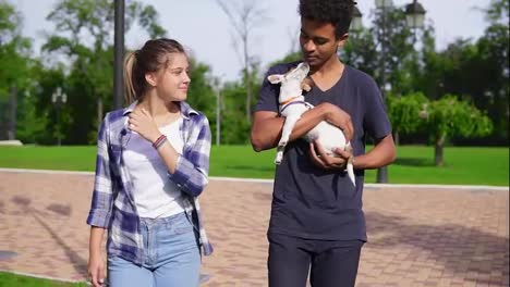 Attractive-multi-ethnic-couple-walking-together-in-park-enjoying-the-day.-African-boy-is-holding-cute-little-jack-russell-terrier