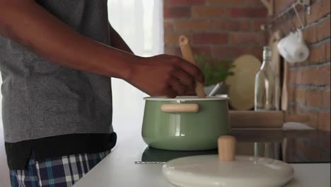 African-man-boiling-water-in-pot-standing-in-the-kitchen,-slow-motion-shot