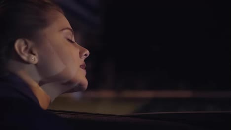 View-from-the-car:-beautiful-young-woman-leaning-out-from-the-car-window-and-looking-at-the-city-at-night.-Slow-Motion-shot