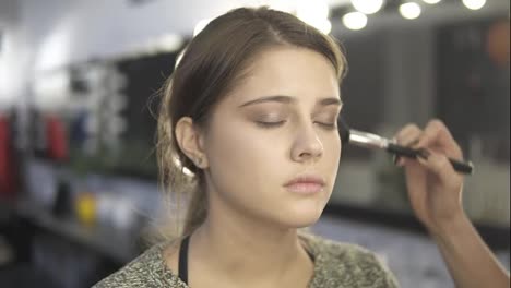 Close-Up-view-of-professional-makeup-artist's-hands-applying-facial-powder-on-young-woman's-skin-using-special-brush.-Slow-Motion
