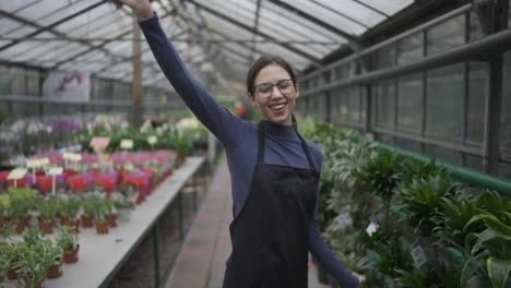 Young-woman-gardener-in-apron-dancing-in-greenhouse