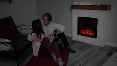 Romantic-young-couple-drinking-red-wine-next-to-the-fireplace