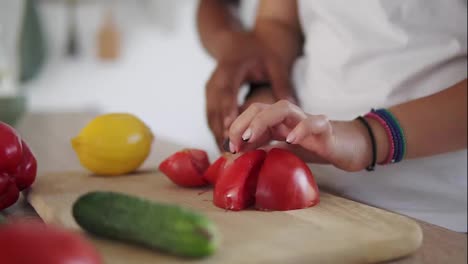 Close-Up-view-of-woman's-hands-cutting-vegetables-while-african-man's-hands-helping-her.-Happy-multi-ethnic-couple-in-the-kitchen