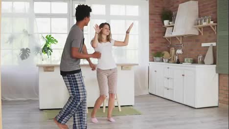 Happy-multiracial-couple-dancing-in-kitchen-wearing-pajamas-listening-to-music-in-the-morning-at-home.-Slow-Motion-shot