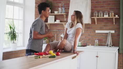Attractive-multi-ethnic-couple-chatting-in-the-kitchen-early-in-the-morning.-Handsome-man-feeding-his-wife-while-cooking