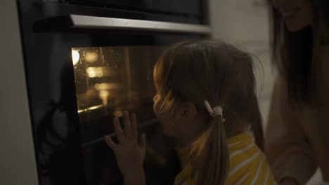 A-little-girl-watches-through-a-glass-how-cookies-are-baked-in-the-oven
