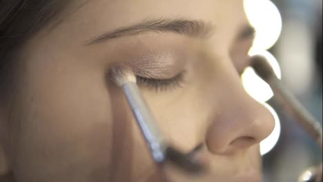 Professional-makeup-artist-using-two-makeup-brushes-to-apply-eye-shadows.-Pro-visagiste-puts-light-brown-shadows-on-eyelid-of-a