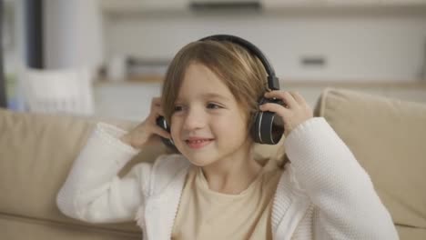 Porträt-Eines-Glücklichen-Kleinen-Mädchens,-Das-Im-Wohnzimmer-Drahtlos-Musik-Mit-Kopfhörern-Hört