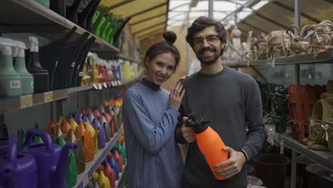 Portrait-of-positive-young-couple-at-the-garden-store-holding-orange-sprayer