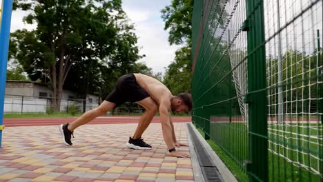 and-athlete-is-doing-push-ups-on-hands-standing-upside-down-near-the-wall-outdoors.-Young-man-topless-in-black-shorts