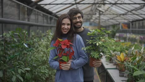 Beautiful-young-couple-in-casual-clothes-both-holding-plants,-looking-at-camera-and-smiling