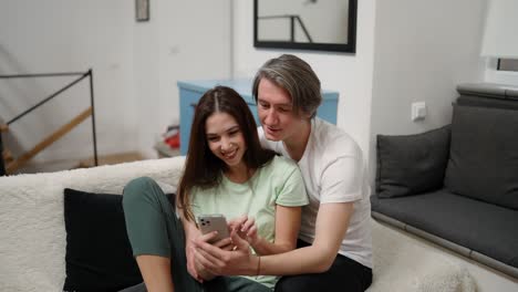 Couple-sit-together-embraced-on-the-bed-using-smartphone,-scrolling-device